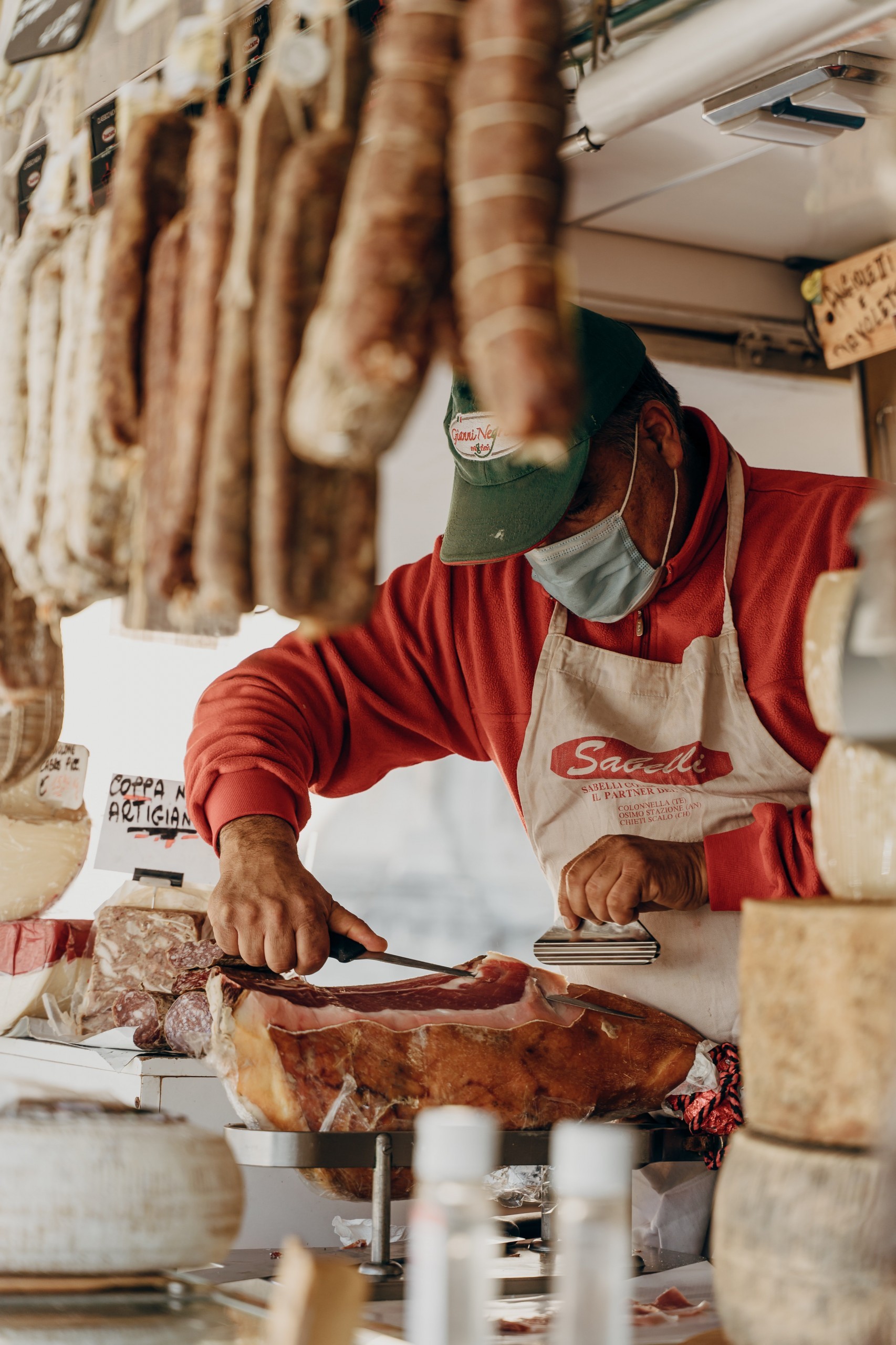 A grocer in Italy cuts a slice from a large block of prosciutto